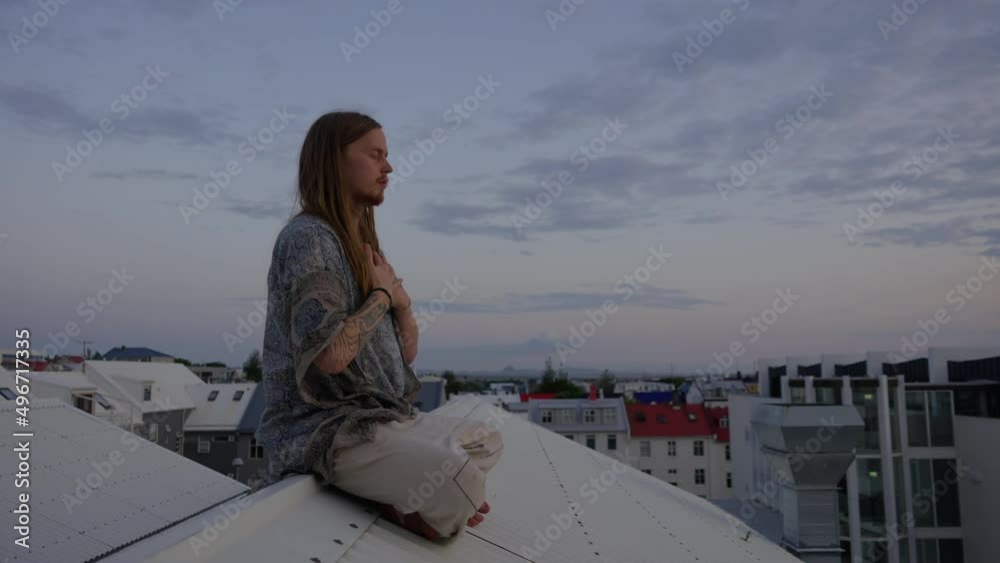 Young Man With Long Hair Meditating On City Roof