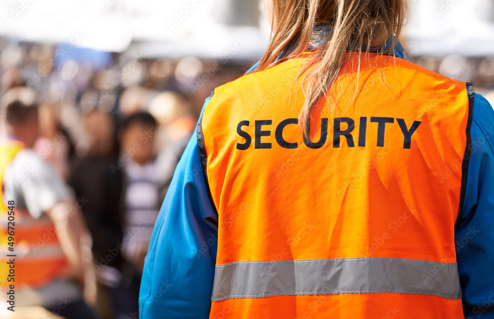 Safety is the main aim. Rearview shot of a security officer standing outdoors with a crowd in the background. Safety is the main aim. Rearview shot of a security officer standing outdoors with a crowd in the background.