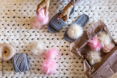 Woman hands connected fluffy fur pom pom to handmade ribbon yarn knitted slippers before sending