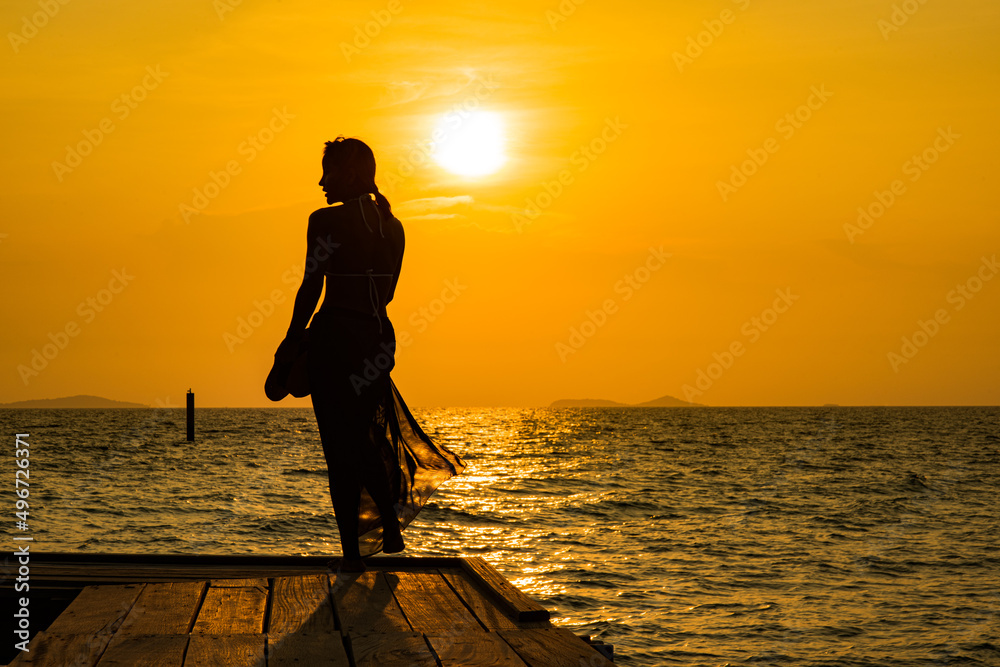 Silhouette young woman on wood bridge with sunset. cheering happy woman open arms to sunrise at seaside.