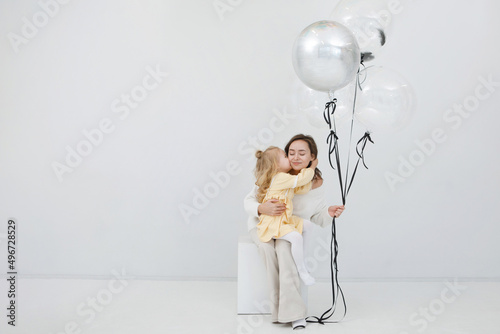 Woman with blonde daughter in white studio with balloons. Festive decoration. Children's happiness. Valentine's Day.