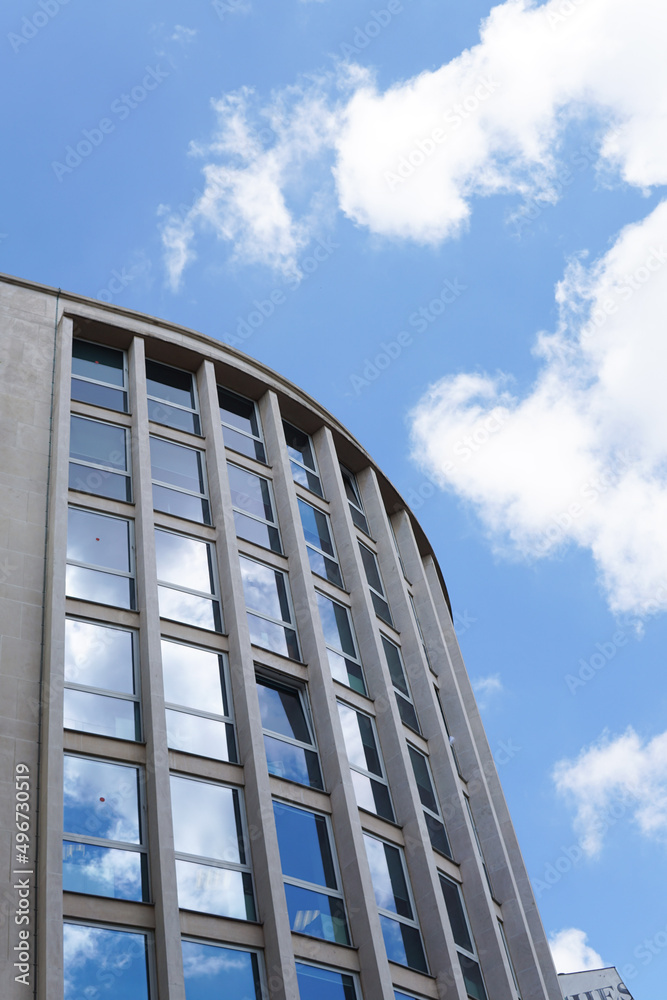 Paris, France - June 6 2019 - The reflection of a blue sky with clouds in the windows of a curved, reflective, office building.  Image has copy space.