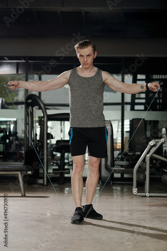 Fit serious young man doing exercise with resistance band in gym