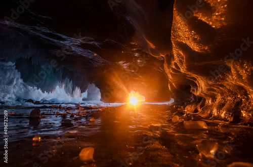 Ice cave on Baikal lake in winter during sunset. Sun reaches ice cave. Orange and blue ice. Beautiful winter feature