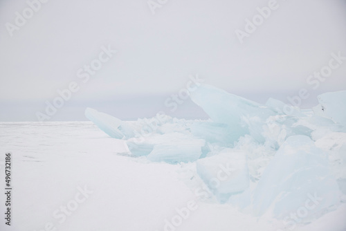 Picturesque ice hummock on winter lake Baikal. Beautiful winter landscape with ice and snow. Horizon, cracked ice, high key, white sky photo