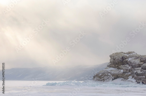 A beautiful cliff surrounded by frozen ice and hummocks seen on frozen winter lake Baikal with mountainous background during sunset. Art photo landscape, winter landscape, beautiful colourful fog