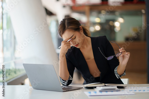 Overworked and stressed young Asian woman sitting at workplace in office.