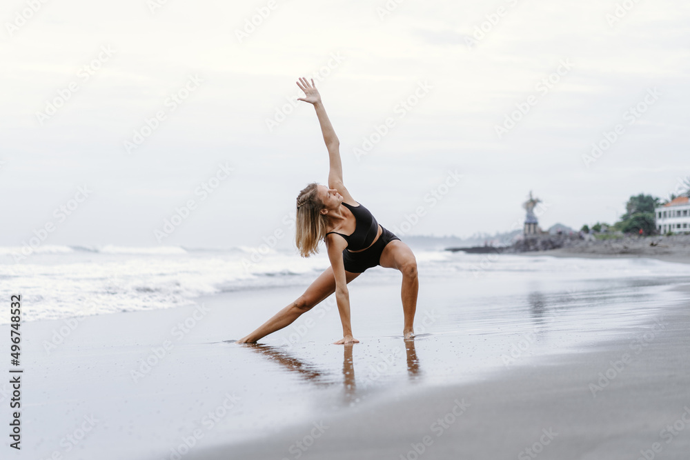 Obraz premium Sporty woman doing mountain climber exercise - run in plank to burn fat. Sunset beach, blue sky background. Healthy lifestyle at tropical island yoga retreat, outdoor activity, family summer vacation.