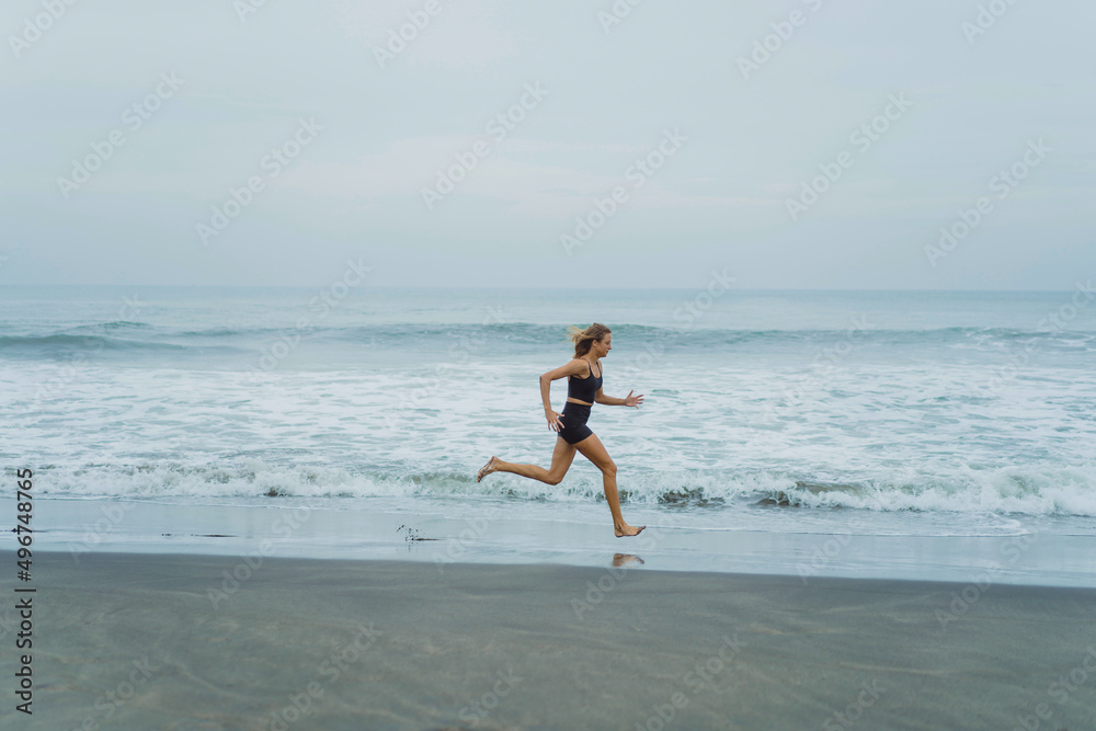 A barefoot young woman with a slender body runs on the sea surf by the water pool to keep fit and burn fat. Women's fitness, jogging, sports activities on a summer.