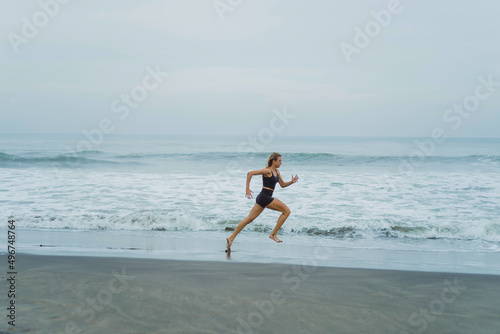 A barefoot young woman with a slender body runs on the sea surf by the water pool to keep fit and burn fat. Women's fitness, jogging, sports activities on a summer.