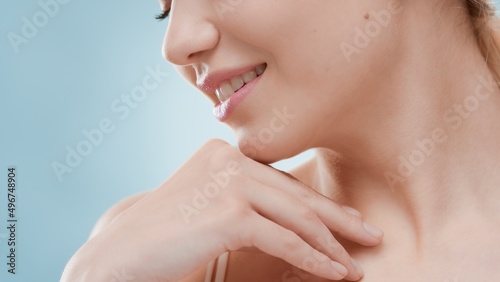 Extreme close up of young Caucasian woman touches her collar bone and turns her head aside against blue background   Beauty care concept