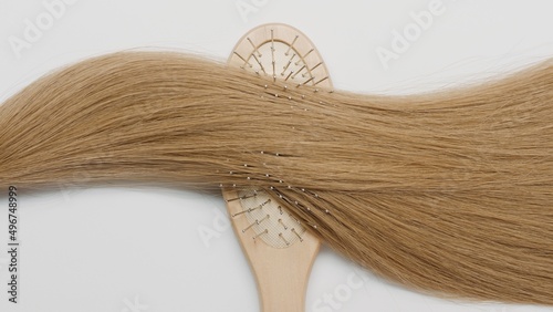 Lock of honey brown hair on brush comb on grey background | Hair treatment concept