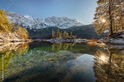 Verschneite Bergwälder und das Wetterstein-Bergmassiv in der Nachmittagssonne spiegeln sich im türkisfarbenen Wasser des Eibsees, Bayern, Deutschland photo