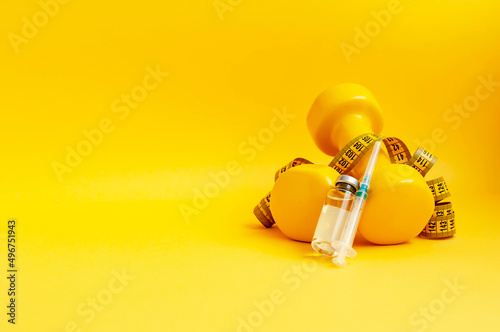 syringe and a jar of liquid lie on dumbbells with a measuring tape on a yellow background, copy space. the concept of doping in sports, steroids, testosterone and other drugs for weight loss.