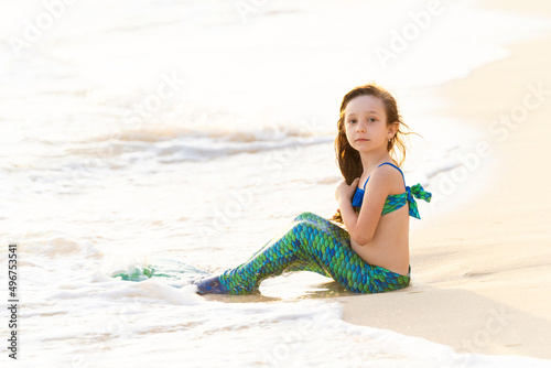 Fotografie A little girl 6 years old in a mermaid costume sits on the sea coast