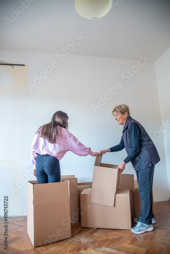 Moving to a new home concept. Young girl in a cardboard box smiling happy to her grandmother.