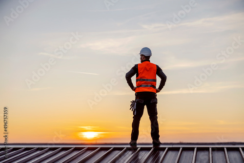 A proud construction worker standing on the roof and looking at twilight.