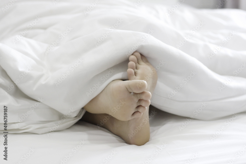 Soles of young women's feet on the bed and white blankets Stock Photo