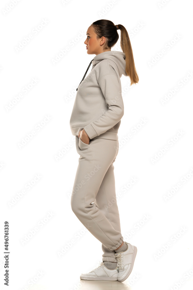 a young woman in a gray tracksuit and pony tail posing to a white background in the studio