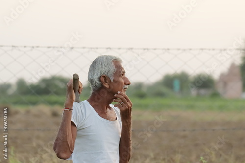 An Indian senior aged man farmer thinking about something while holding a shovel in his hand at sunset