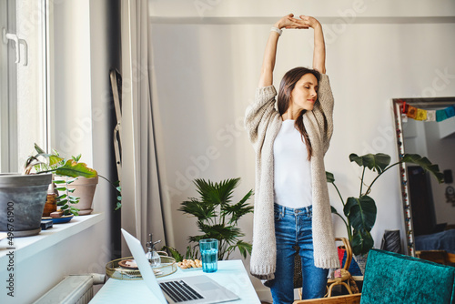 Freelancer stretching arms standing by desk at home office