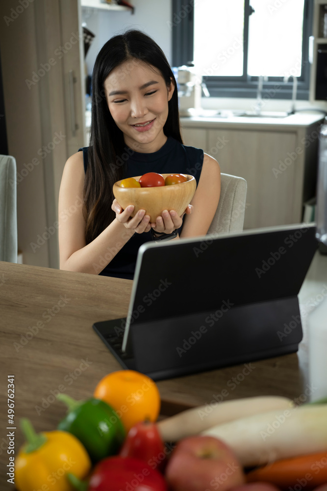 Pretty millennial woman preparing ingredients for making healthy salad and looking online recipe on digital tablet.