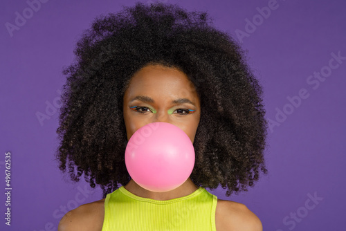 Beautiful young woman blowing pink bubble gum against purple background photo