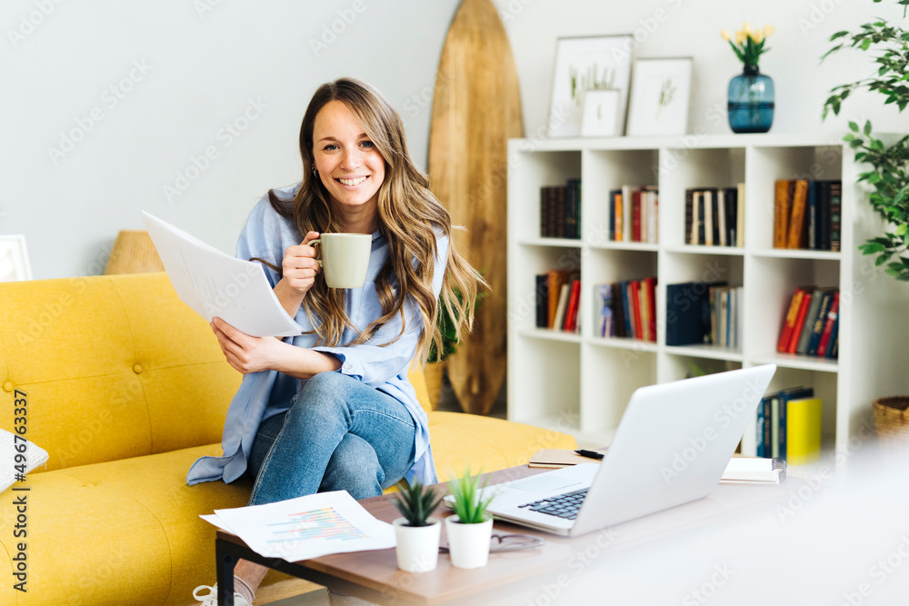 Happy freelancer with documents and coffee cup sitting on sofa at home Happy freelancer with documents and coffee cup sitting on sofa at home