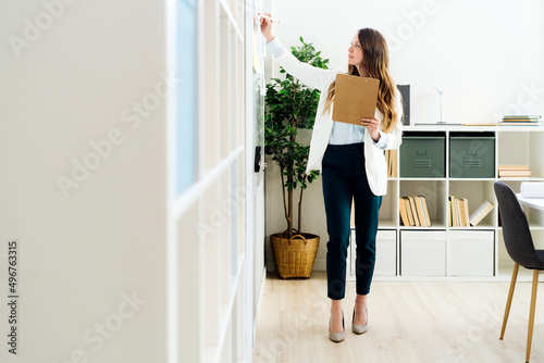 Businesswoman holding file folder writing on whiteboard in office