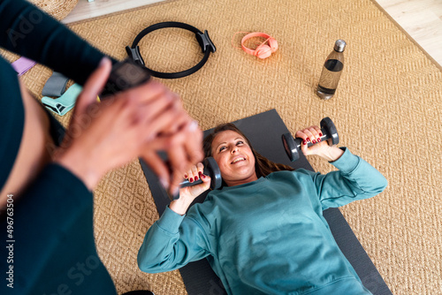 Smiling woman exercising with dumbbells looking at friend in living room photo