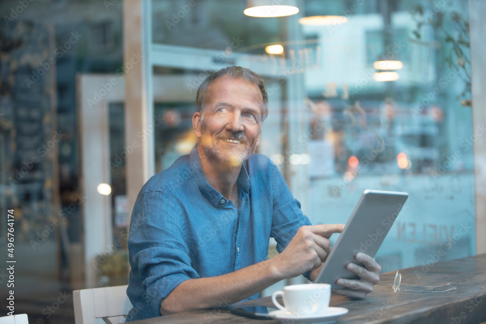 Smiling businessman with tablet PC sitting at table by window in cafe Smiling businessman with tablet PC sitting at table by window in cafe