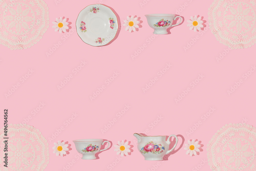 Spring creative frame with vintage tea cups, saucers, embroidery lace placemat and flower heads on pastel pink background. 80s, 90s retro romantic aesthetic summer concept. Fashion tea party idea.