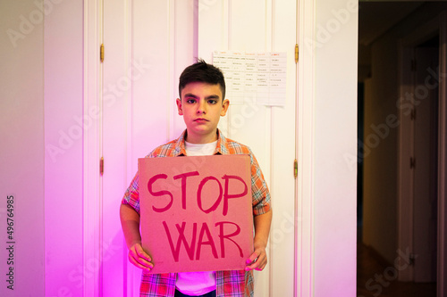 Boy with stop war placard standing in front of door at home photo