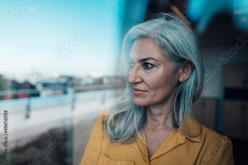 Thoughtful businesswoman with gray hair seen through glass photo