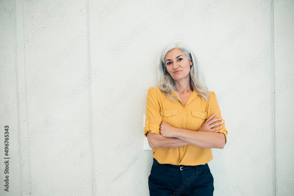Smiling businesswoman standing with arms crossed in front of wall Smiling businesswoman standing with arms crossed in front of wall