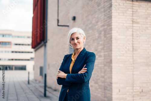 Smiling business person standing with arms crossed outside office building photo