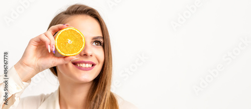 Portrait of a cheerful caucasian young woman covering eye with an orange slice wearing a white shirt over a white background