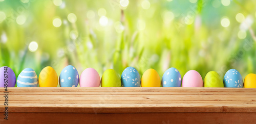 Photography Easter holiday background with empty wooden table and Easter eggs over green grass meadow