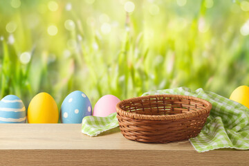 Empty basket with tablecloth and Easter eggs on wooden table over green bokeh background. Easter mock up for design and product display.