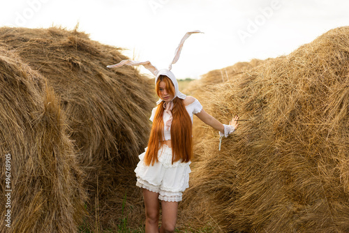 Young woman wearing rabbit costume ears standing amidst hay bales photo