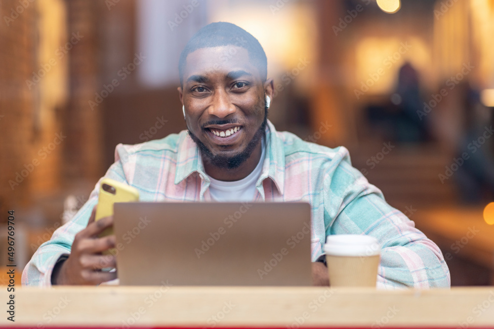 Happy man with laptop and smart phone sitting in cafe seen through glass