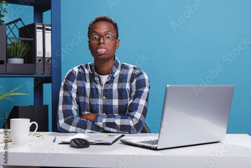 Fotografie Funny and goofy office working person making amusing playful face while sticking out tongue