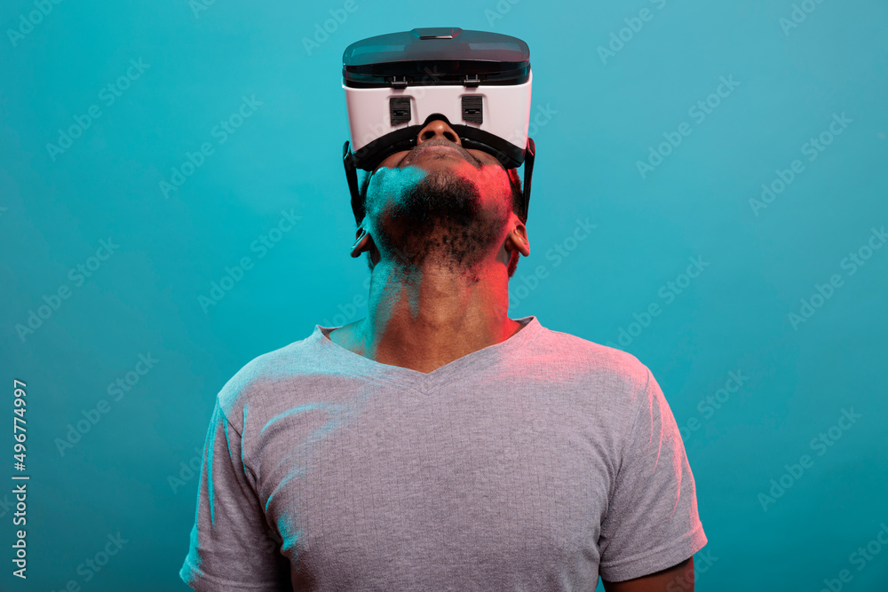 Male model looking up while he uses virtual reality glasses with interactive technology and 3d visual. Person using vr goggles with futuristic simulation to have fun experience in studio. Male model looking up while he uses virtual reality glasses with interactive technology and 3d visual. Person using vr goggles with futuristic simulation to have fun experience in studio.