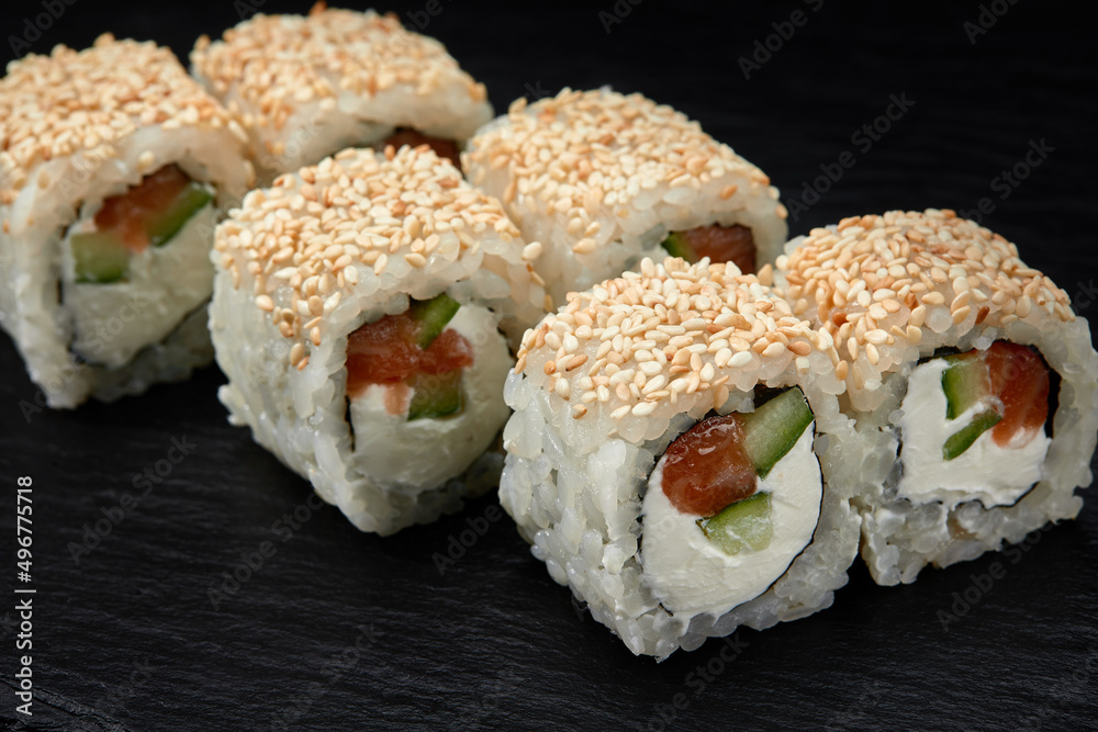 Traditional delicious fresh sushi roll set on a black background. Sushi roll with rice, cream cheese, avocado, salmon, sesame. Philadelphia. Sushi menu. Japanese kitchen, restaurant. Traditional delicious fresh sushi roll set on a black background. Sushi roll with rice, cream cheese, avocado, salmon, sesame. Philadelphia. Sushi menu. Japanese kitchen, restaurant.