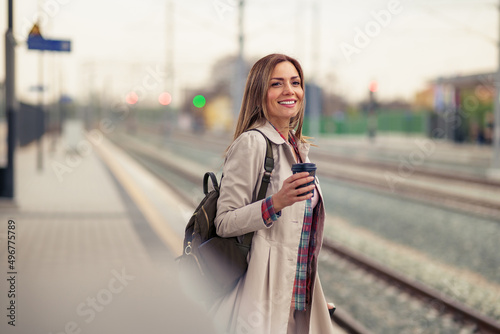 Woman with suitcase waiting for her train on platform of railway station. She is smiling and holding her cup of coffee. © DusanJelicic