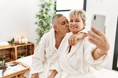 Senior caucasian couple smiling happy making selfie by the smartphone sitting on massage table at beauty center.