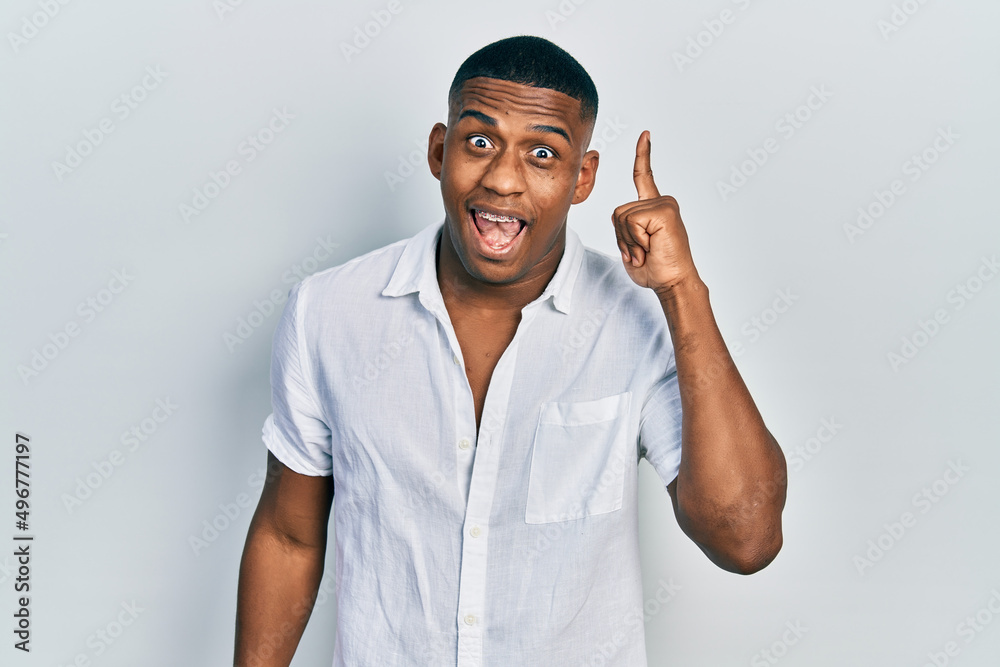 Young black man wearing casual white shirt pointing finger up with successful idea. exited and happy. number one. Young black man wearing casual white shirt pointing finger up with successful idea. exited and happy. number one.