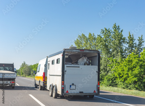 European-style horse box with horses pulled by minibus on hungarian road. Horse trailer on highway.