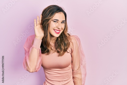 Young hispanic girl wearing casual clothes smiling with hand over ear listening an hearing to rumor or gossip. deafness concept.