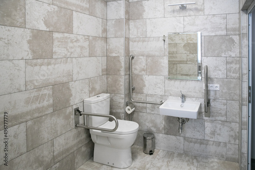 modern bathroom interior with white toilet  handicapped rails  white sink and mirror